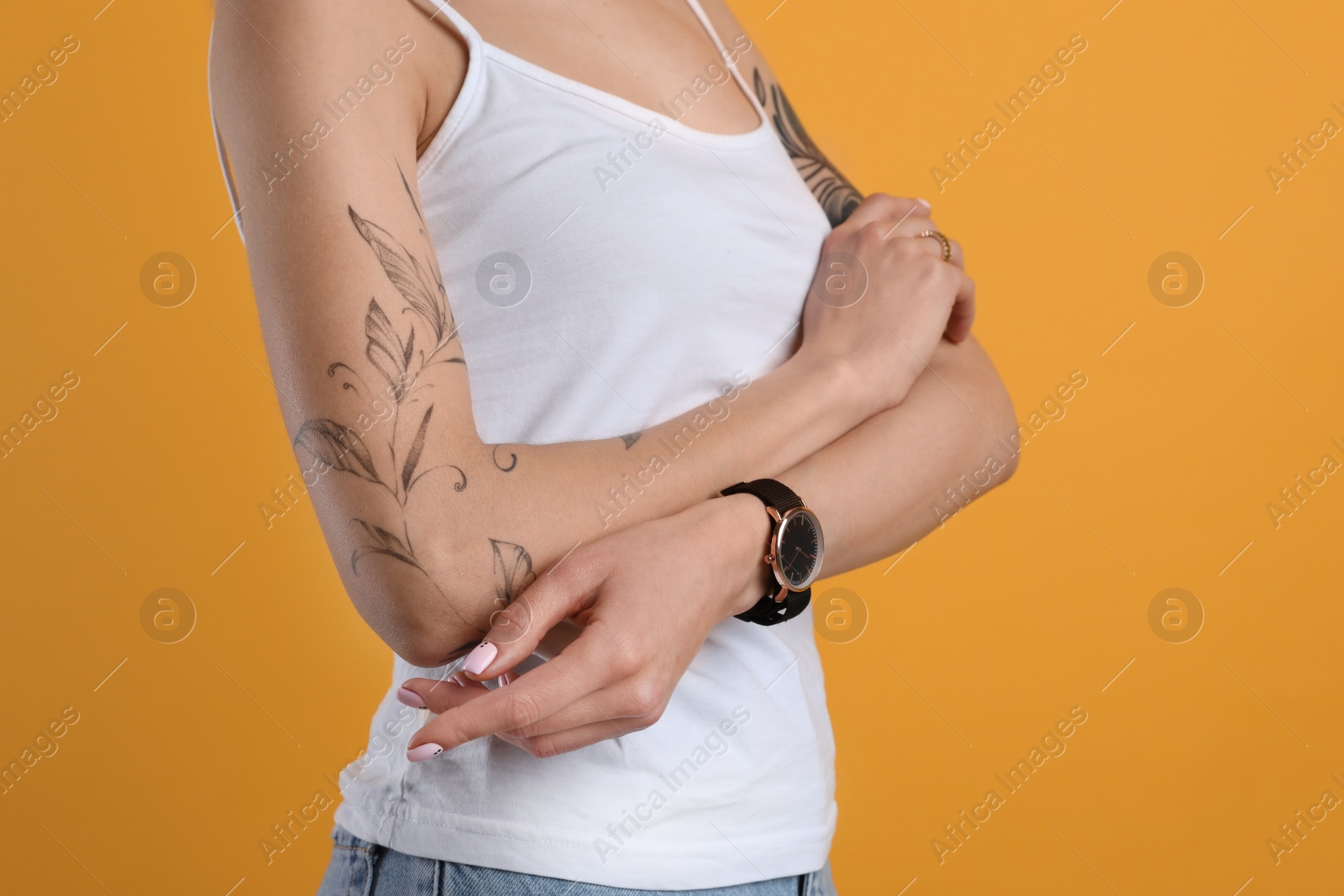 Photo of Beautiful woman with tattoos on arms against yellow background, closeup