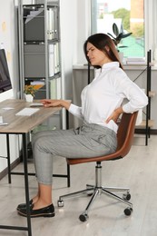 Photo of Young woman suffering from back pain while sitting in office. Symptom of scoliosis