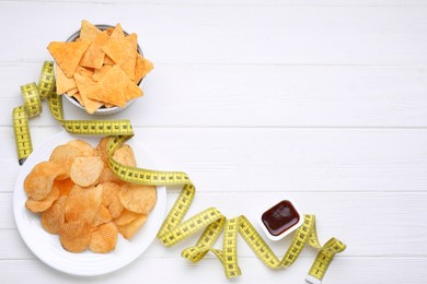 Photo of Potato chips, tomato sauce and measuring tape on white wooden table, flat lay with space for text. Weight loss concept