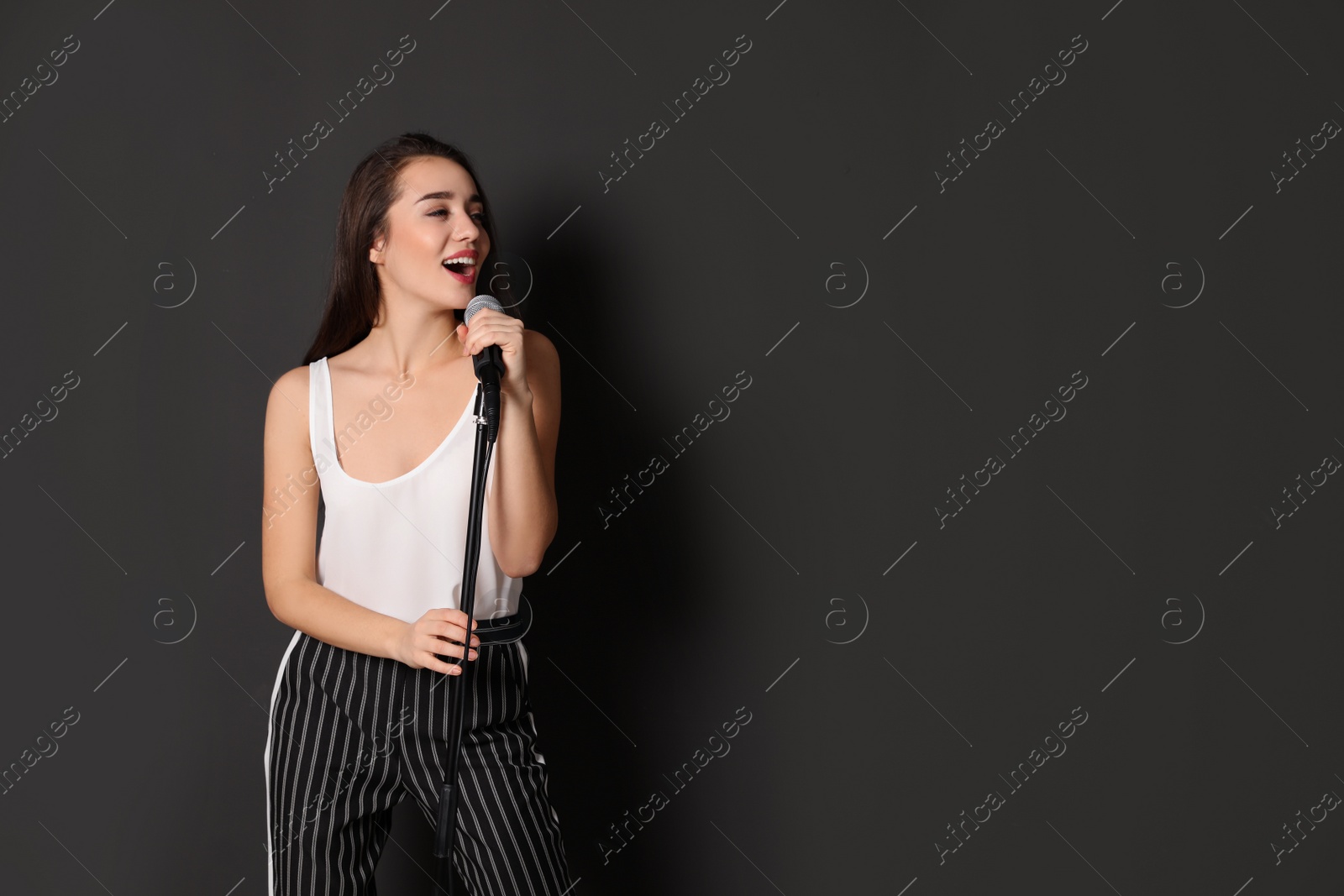 Photo of Young stylish woman singing in microphone on dark background. Space for text