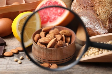 Photo of Different products with magnifier focused on almonds, closeup. Food allergy concept