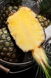 Photo of Whole and cut ripe pineapples in metal basket on black table, top view