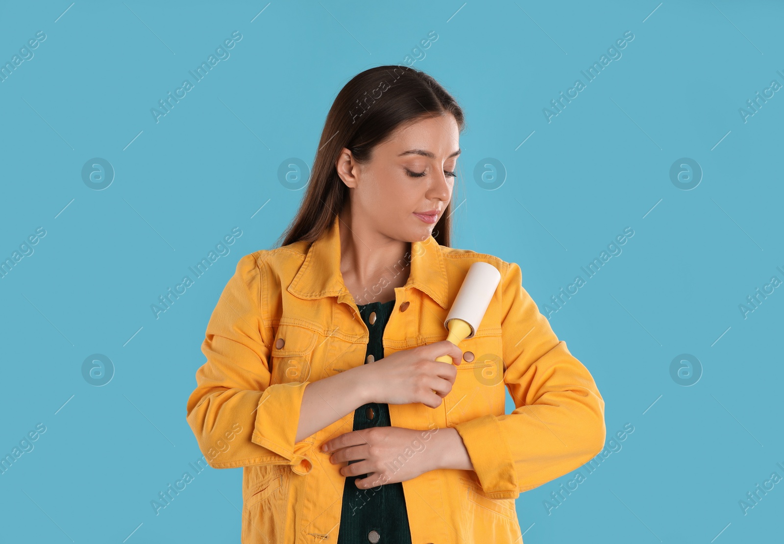 Photo of Young woman cleaning clothes with lint roller on light blue background