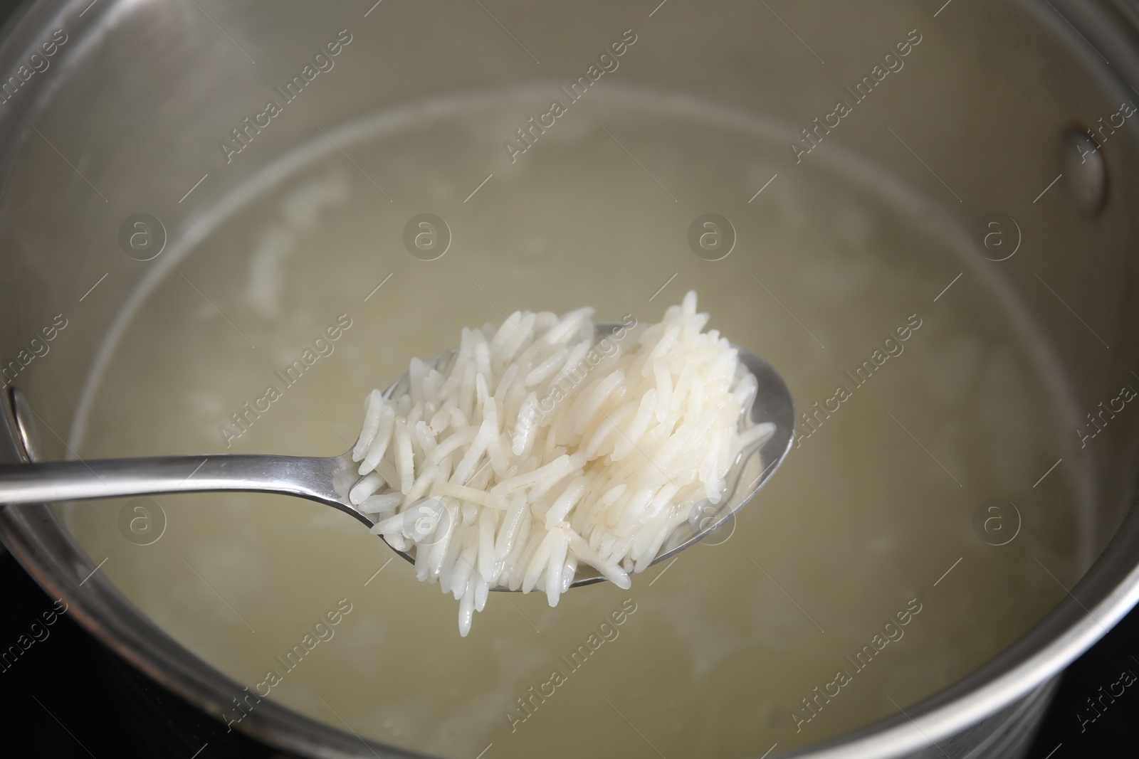 Photo of Spoon with cooked rice over pot, closeup