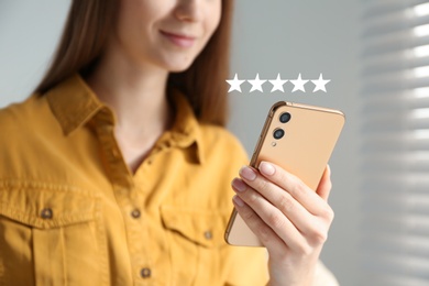 Woman leaving review online via smartphone indoors, closeup. Five stars over gadget