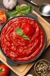 Photo of Homemade tomato sauce in bowl, spoon and ingredients on wooden table, flat lay