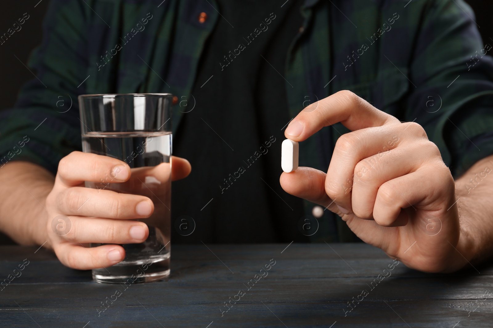 Photo of Man holding pill and glass of water at table, closeup