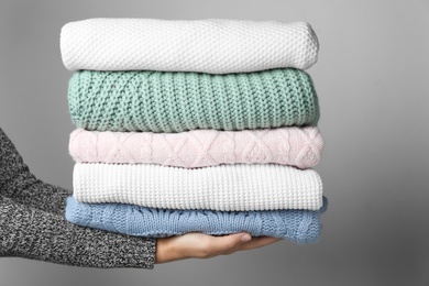 Photo of Woman holding stack of warm clothes on grey background, closeup. Autumn season