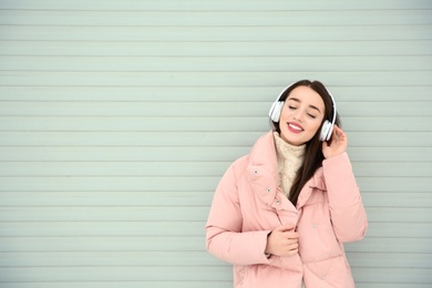 Photo of Beautiful young woman listening to music with headphones against light wall. Space for text