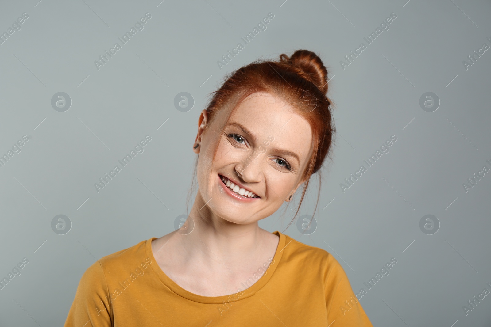 Photo of Candid portrait of happy red haired woman with charming smile on grey background