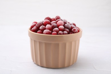 Frozen red cranberries in bowl on white table, closeup