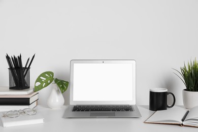 Photo of Cozy workspace with laptop, houseplants and stationery on white desk at home