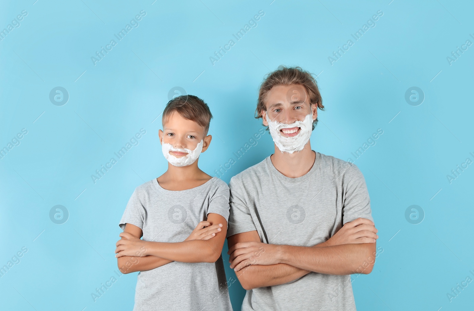 Photo of Father and son with shaving foam on faces against color background