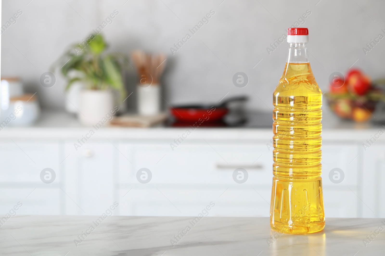 Photo of Bottle of cooking oil on white marble table in kitchen. Space for text