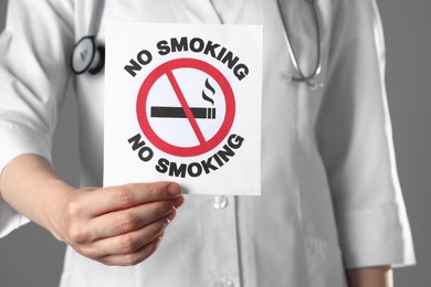 Doctor holding card with no smoking sign on gray background, closeup