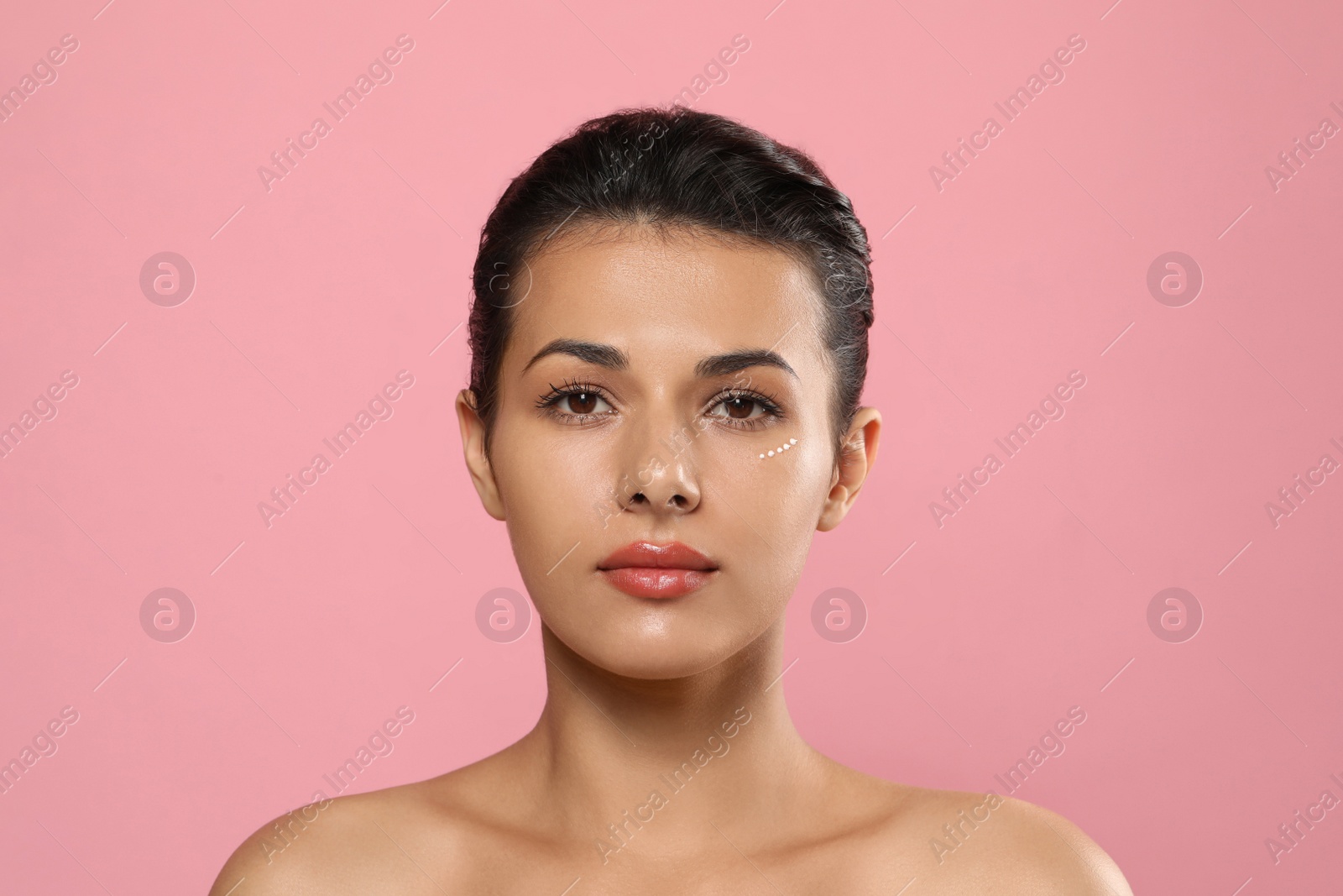 Photo of Woman with cream around eye on pink background. Skin care