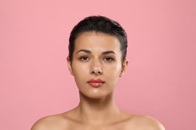 Photo of Woman with cream around eye on pink background. Skin care