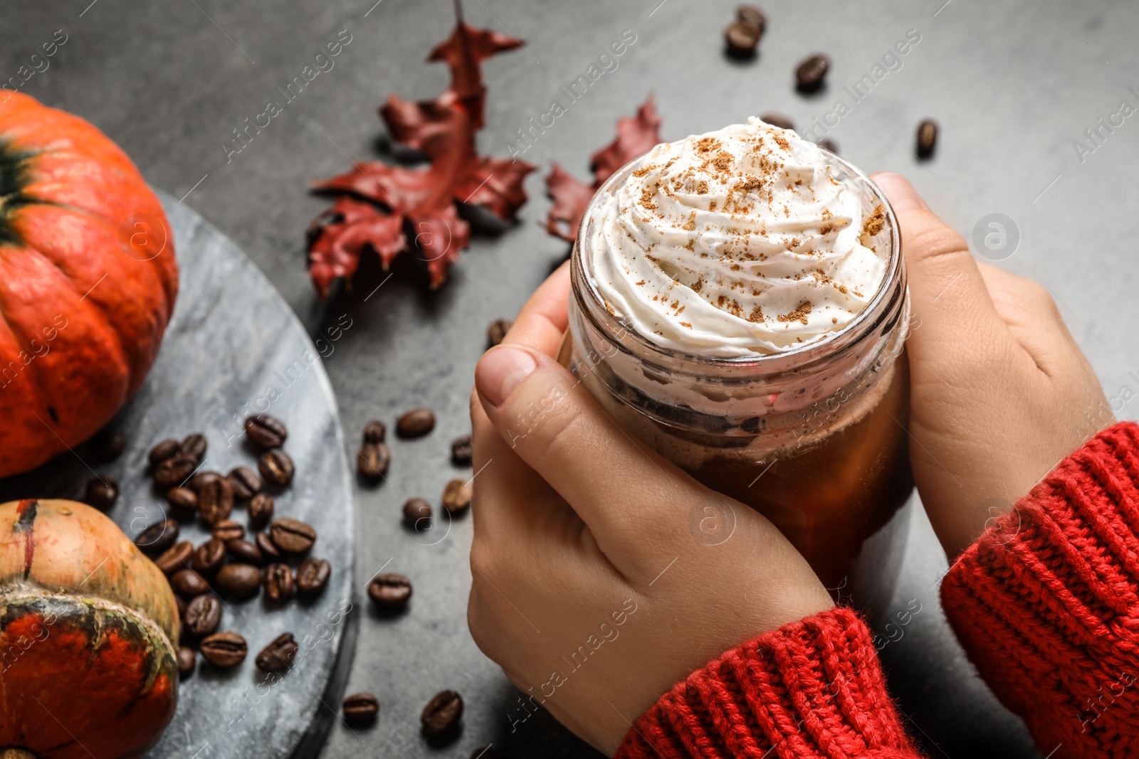 Photo of Woman holding mason jar of tasty pumpkin spice latte at grey table, closeup