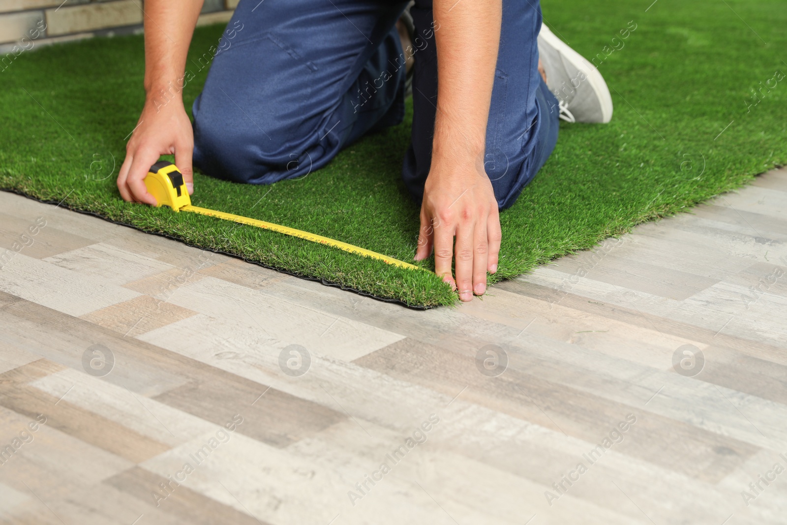 Photo of Man measuring artificial grass carpet indoors, closeup. Space for text