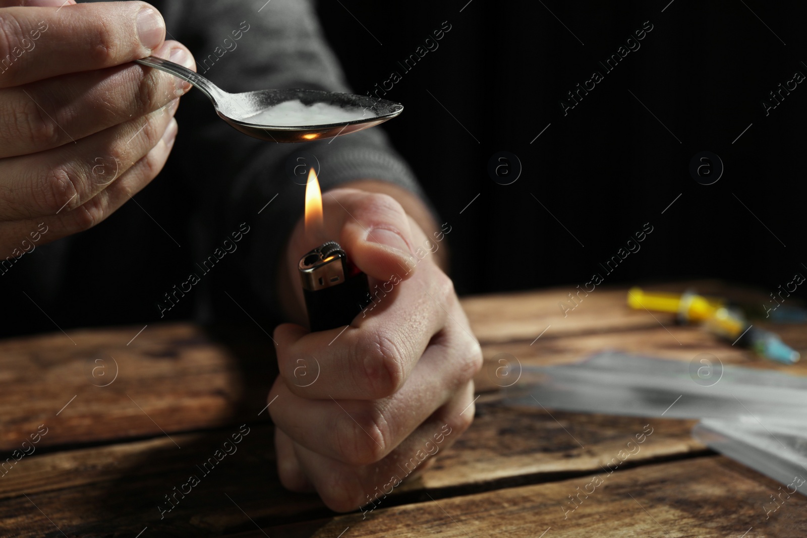 Photo of Man preparing drugs with spoon and lighter at wooden table, closeup. Space for text