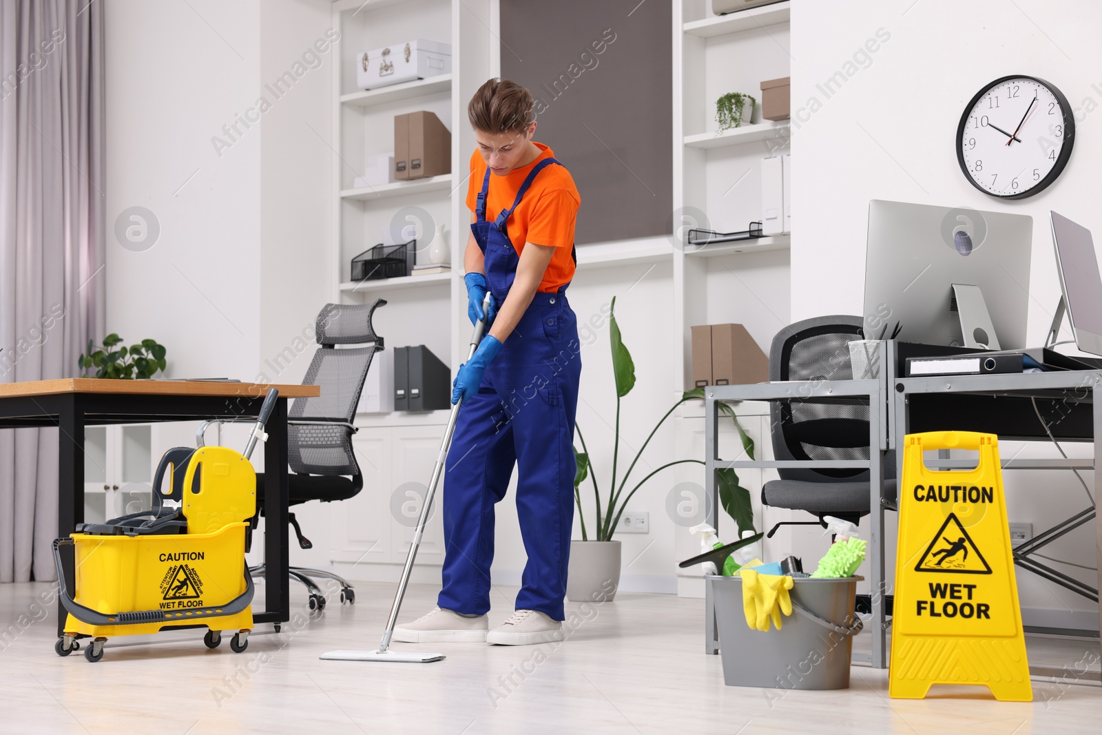 Photo of Cleaning service worker washing floor with mop. Bucket with supplies and wet floor sign in office