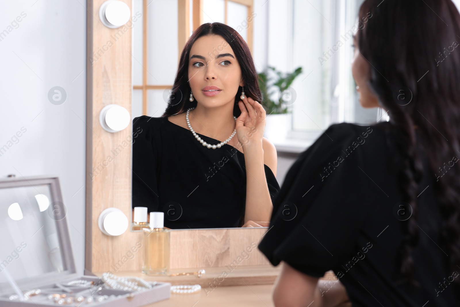 Photo of Young woman wearing elegant pearl jewelry near mirror indoors