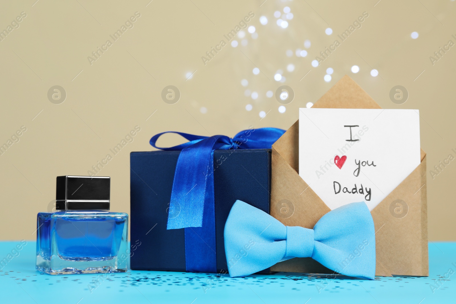 Photo of Happy Father's Day. Card with phrase I Love You, Daddy in envelope, bow tie, perfume and gift box on light blue table, closeup