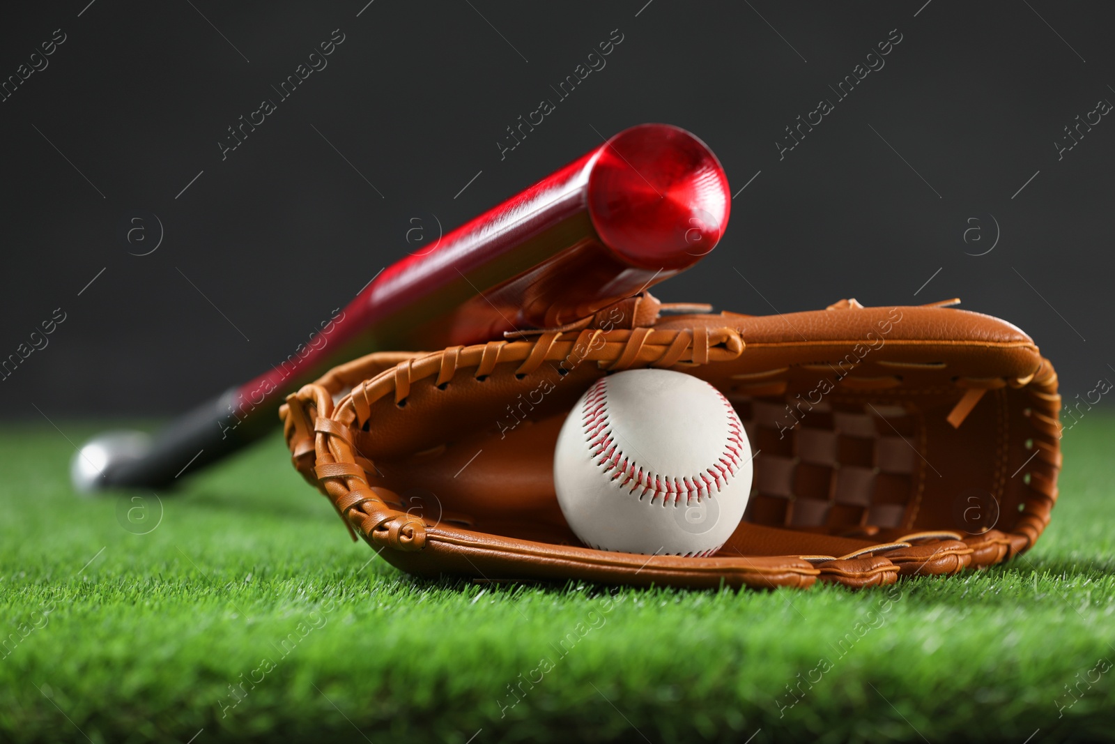 Photo of Baseball bat, leather glove and ball on green grass against dark background, closeup