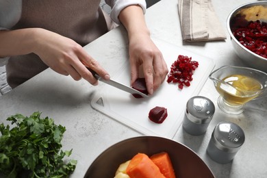 Photo of Woman cutting boiled beetroot at white table, closeup. Cooking vinaigrette salad