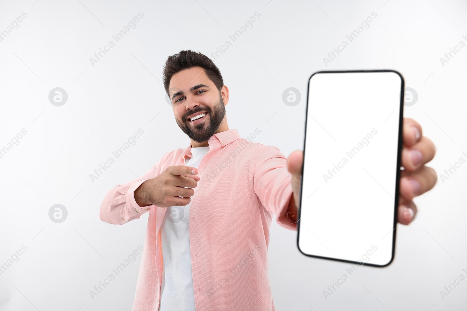 Photo of Young man showing smartphone in hand and pointing at it on white background