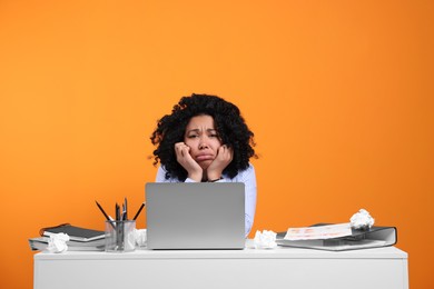 Stressful deadline. Exhausted woman sitting at white desk against orange background