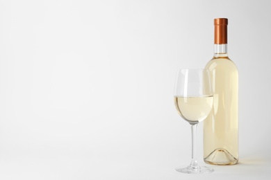 Bottle and glass of expensive white wine on light background