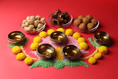 Happy Diwali. Diya lamps, colorful rangoli, flowers and delicious Indian sweets on red table