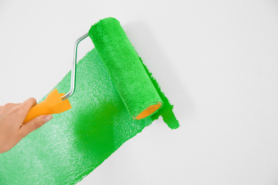 Photo of Woman painting white wall with green dye, closeup. Interior renovation