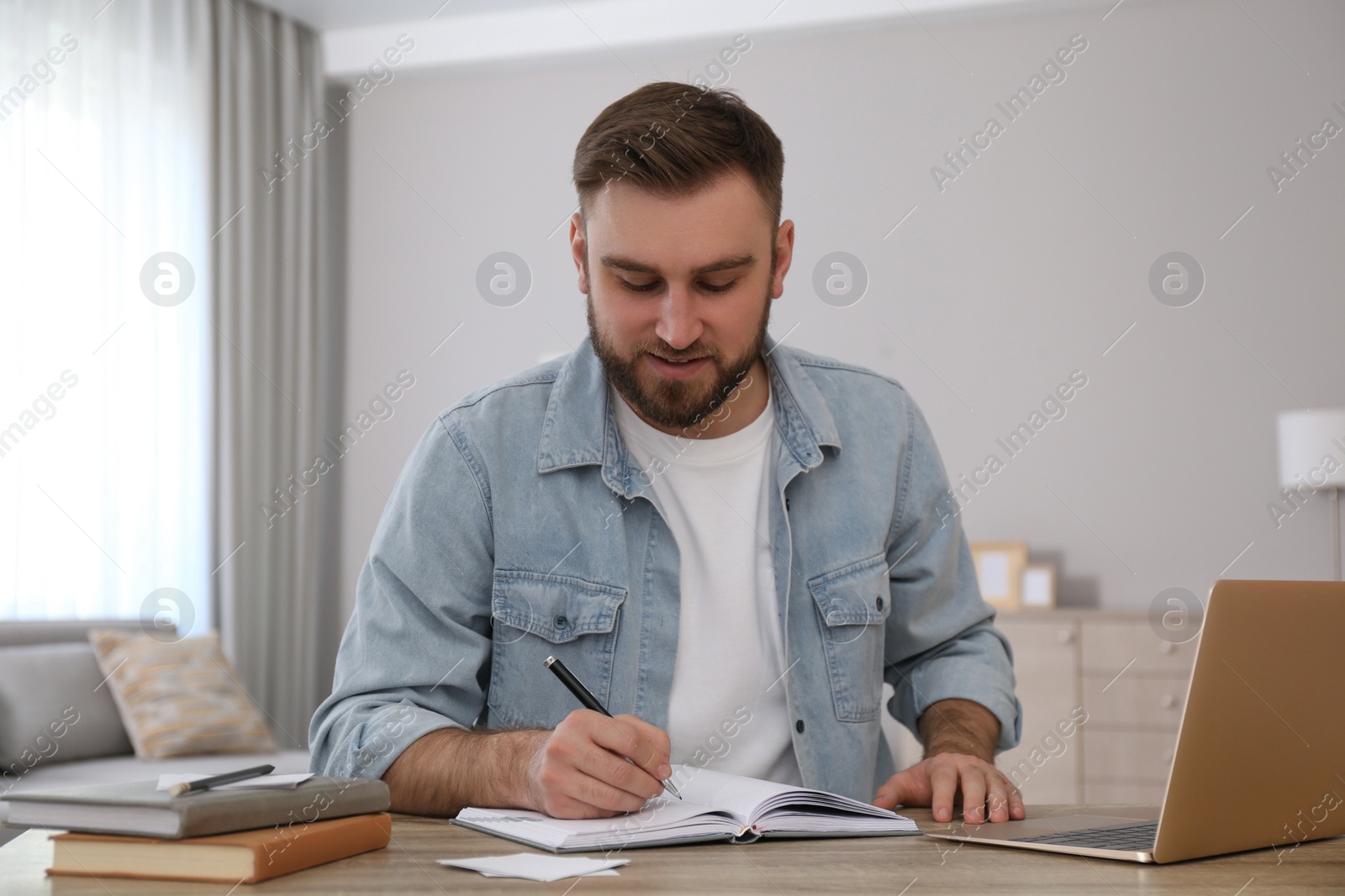 Photo of Young man taking notes during online webinar at table indoors