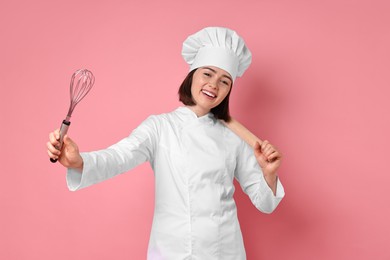 Happy confectioner with rolling pin and whisk on pink background