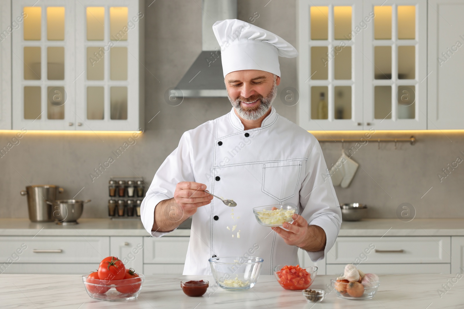 Photo of Professional chef making delicious tomato sauce at white marble table indoors