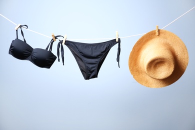 Stylish bikini and hat hanging on rope against color background