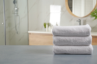 Photo of Stack of clean towels on grey stone table in bathroom. Space for text