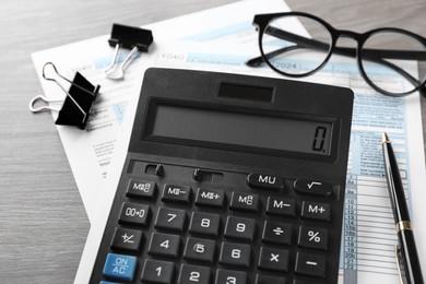 Tax accounting. Calculator, documents, glasses and stationery on wooden table, closeup