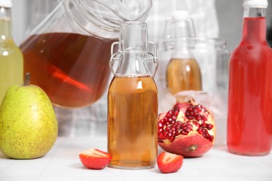 Pouring tasty kombucha into glass bottle at white table, closeup