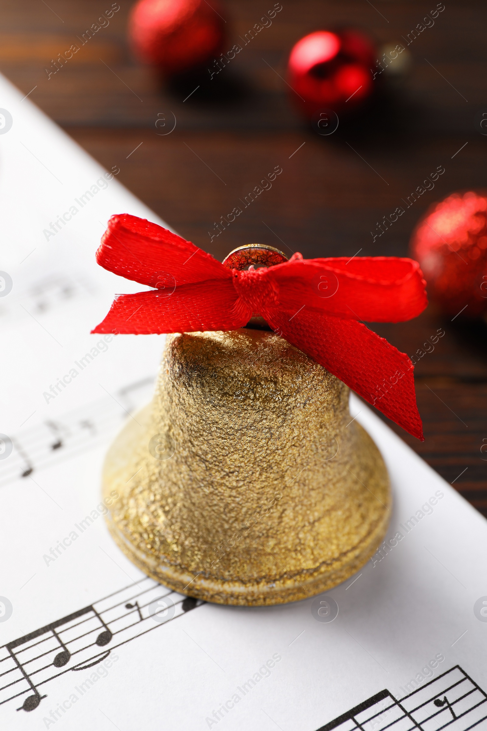 Photo of Golden shiny bell with red bow and music sheet on table, closeup. Christmas decoration