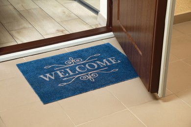 Photo of Beautiful blue doormat with word Welcome on floor near entrance