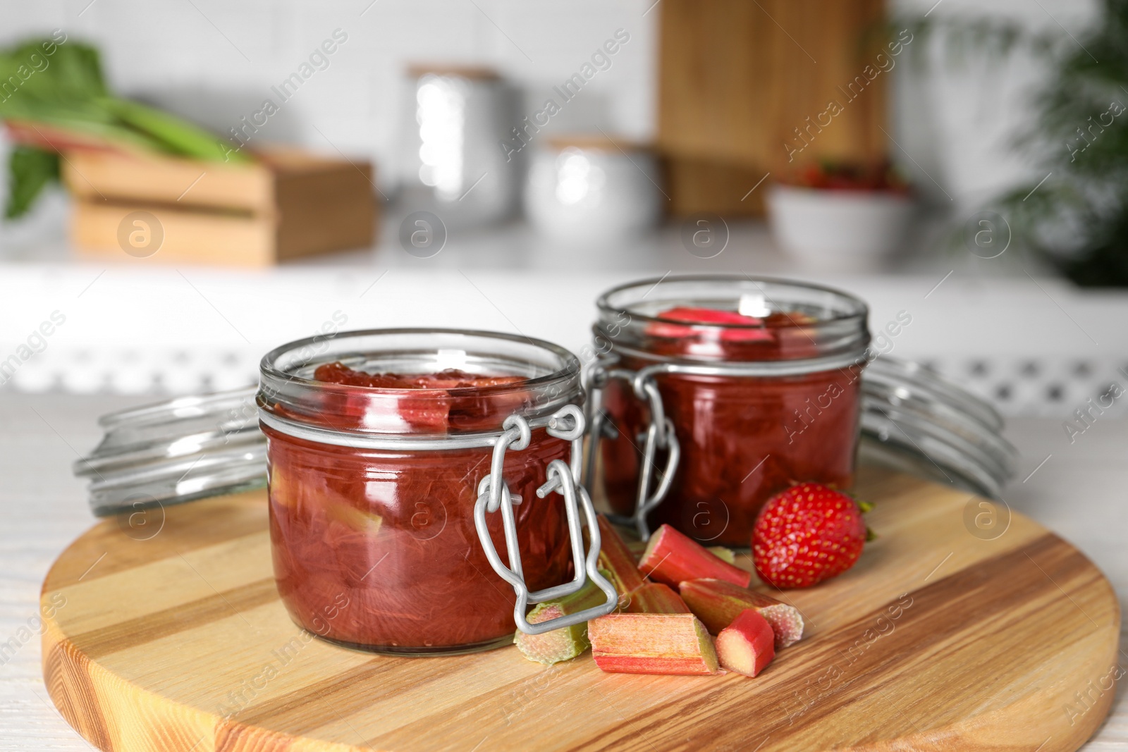 Photo of Jars of tasty rhubarb jam, cut stems and strawberry on white table