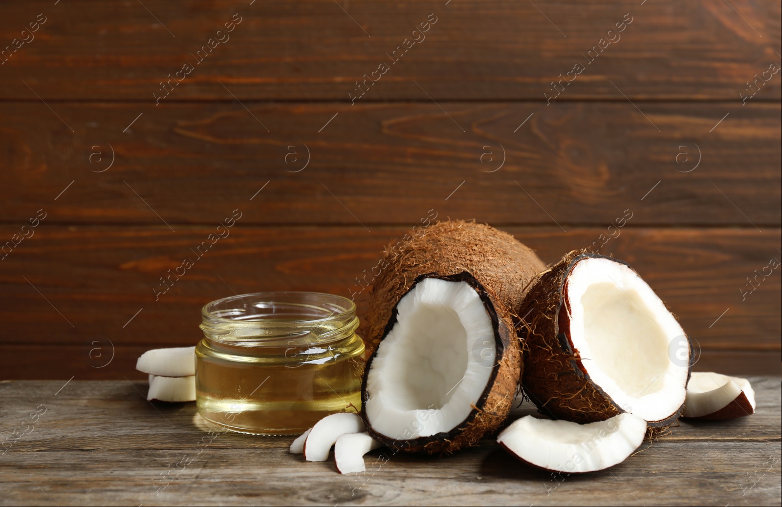 Photo of Jar of natural organic oil and coconuts on brown wooden table