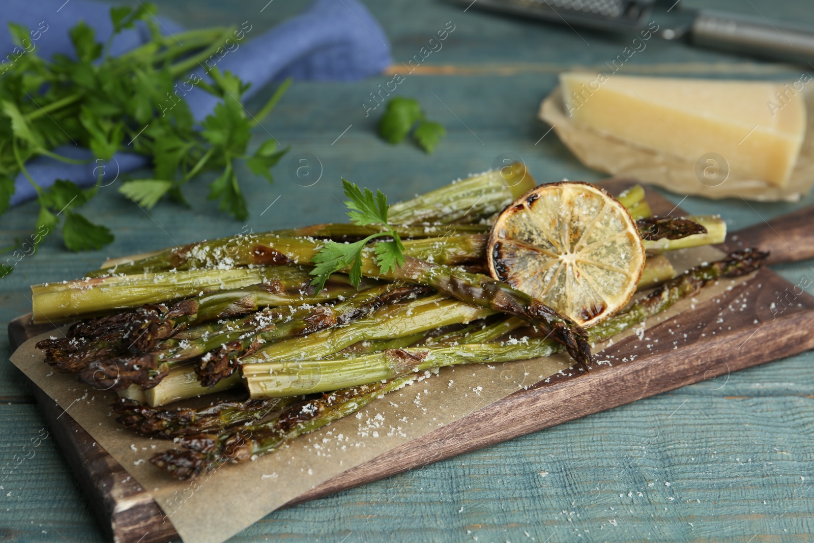 Photo of Oven baked asparagus served with lemon and parsley on blue wooden table