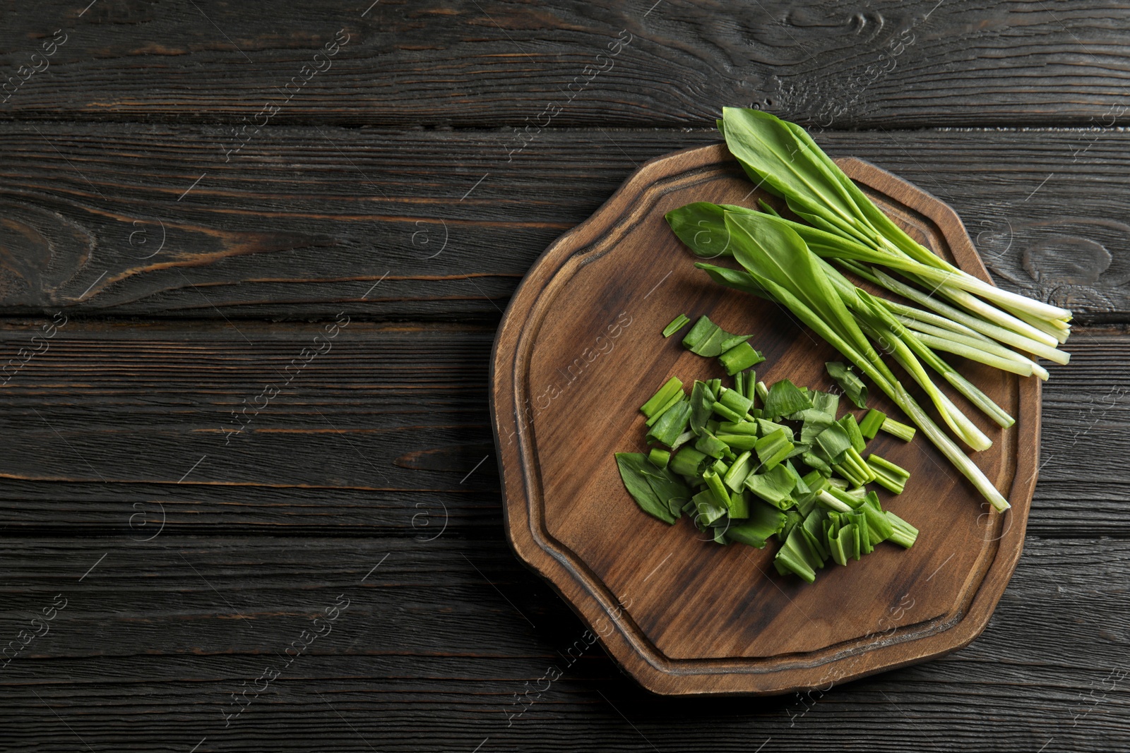 Photo of Board with wild garlic or ramson on wooden table, top view. Space for text