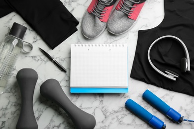 Photo of Flat lay composition with sportswear, notebook and dumbbells on white marble background. Gym workout plan
