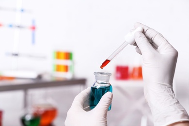 Photo of Scientist dripping reagent into bottle with sample in chemistry laboratory, closeup. Space for text