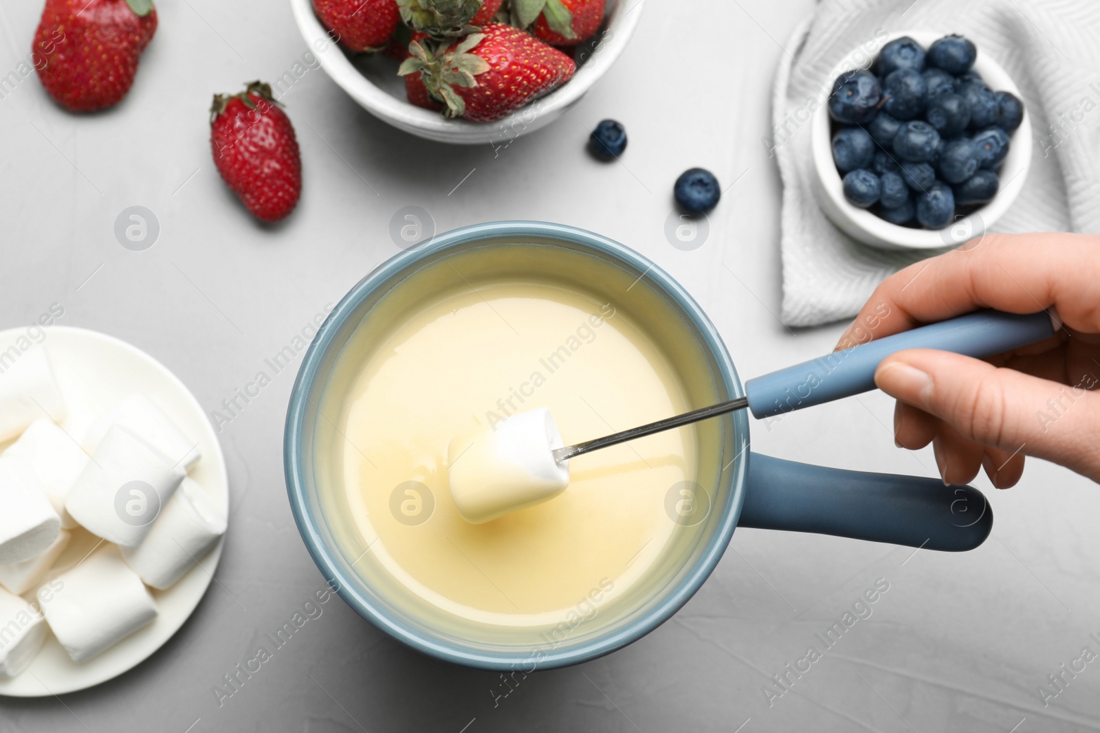 Photo of Woman dipping marshmallow into pot with white chocolate fondue at table, top view